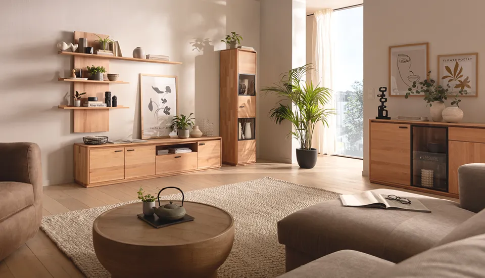 Gemütliches Wohnzimmer mit massiven Holzmöbeln, offener Wandregalgestaltung, Glasvitrine und grünen Pflanzen, sorgt für warme, natürliche Atmosphäre in modernem Einrichtungsstil.